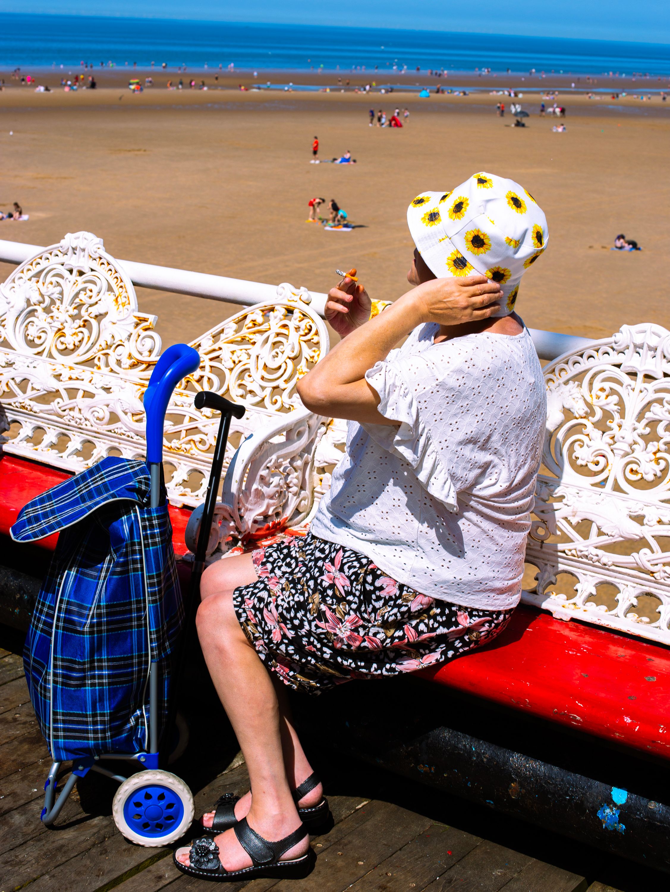 A woman smoking on a pier near a beach.