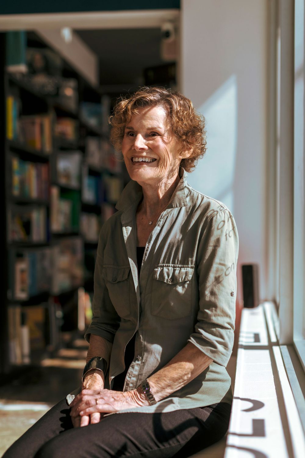 Judy Blume sitting by the window in a bookstore.