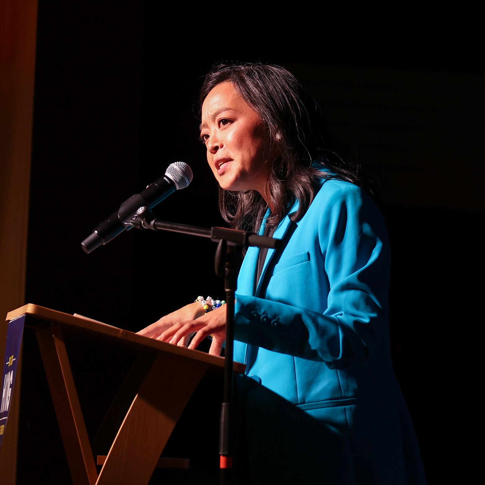 Figure stands at a podium and speaks into a microphone.
